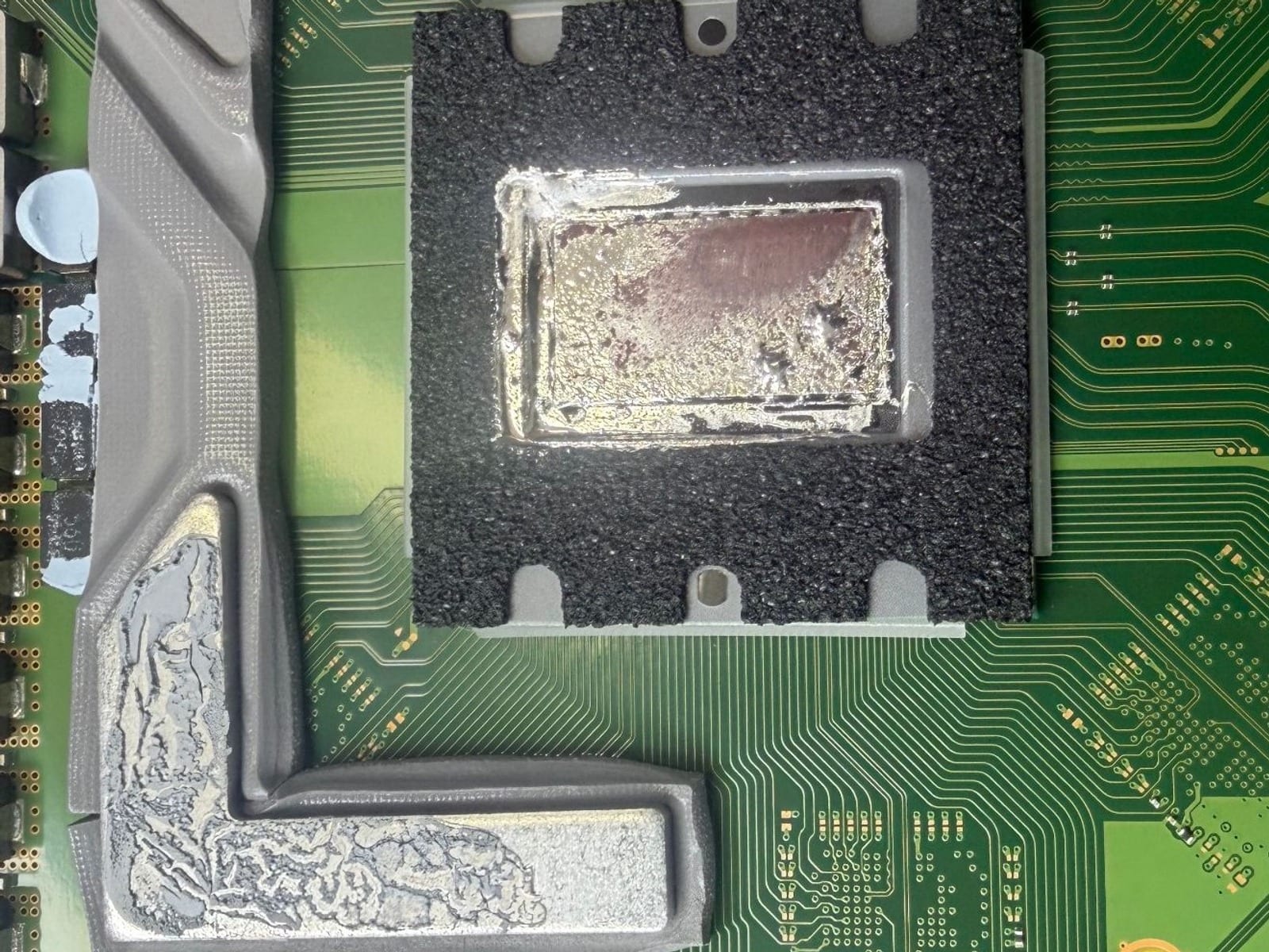 The processor on a PlayStation 5 motherboard at MTM IT, with the liquid metal thermal compound dried and migrated away from the centre of the die and pooled along the metal shield frame beside it